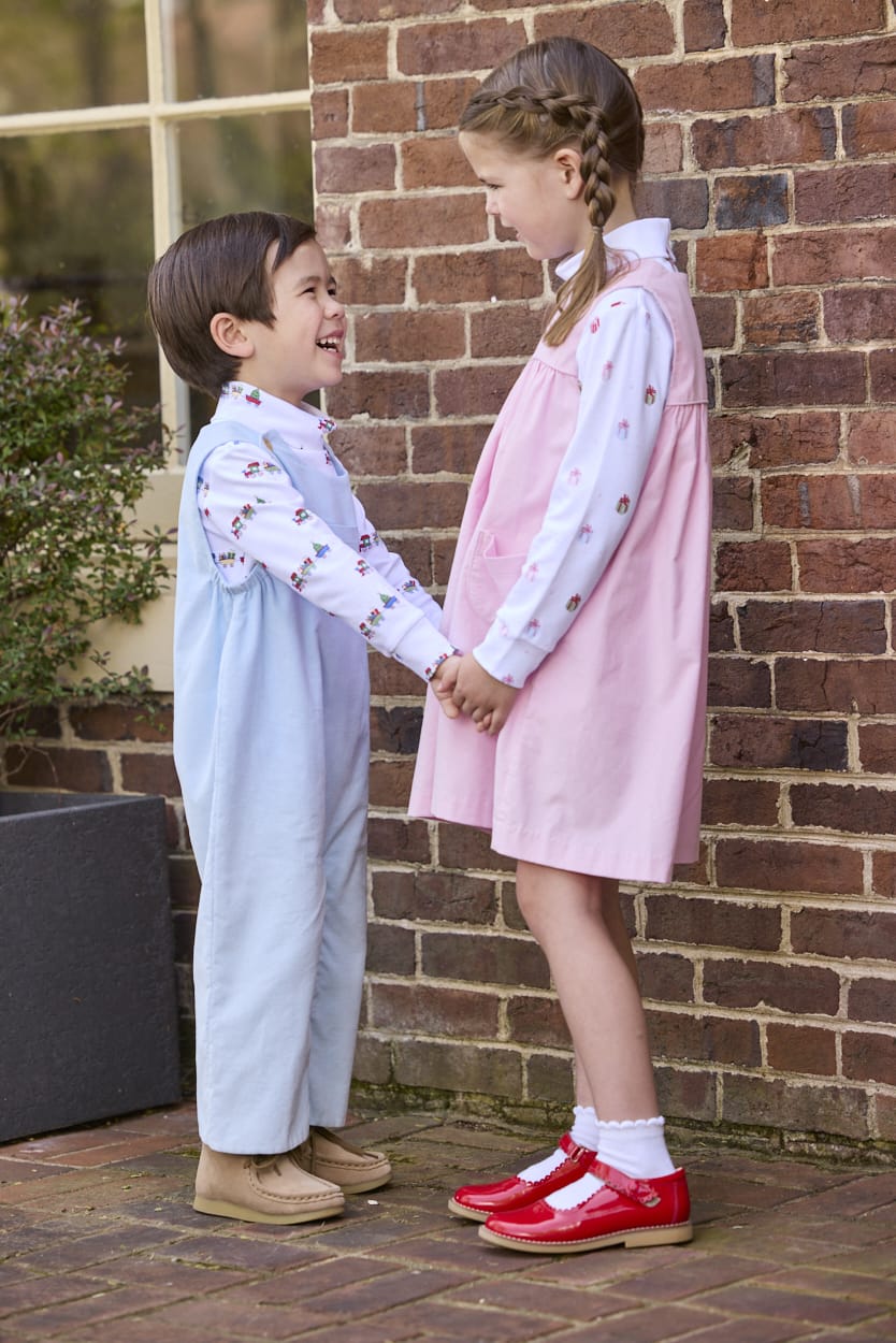 Little English classic children's clothing. White knit turtleneck with holiday train print layered under light blue corduroy Campbell Overall. White knit turtleneck with holiday present print layered under light pink corduroy Madison Jumper. Holiday outfit for little boys and girls.