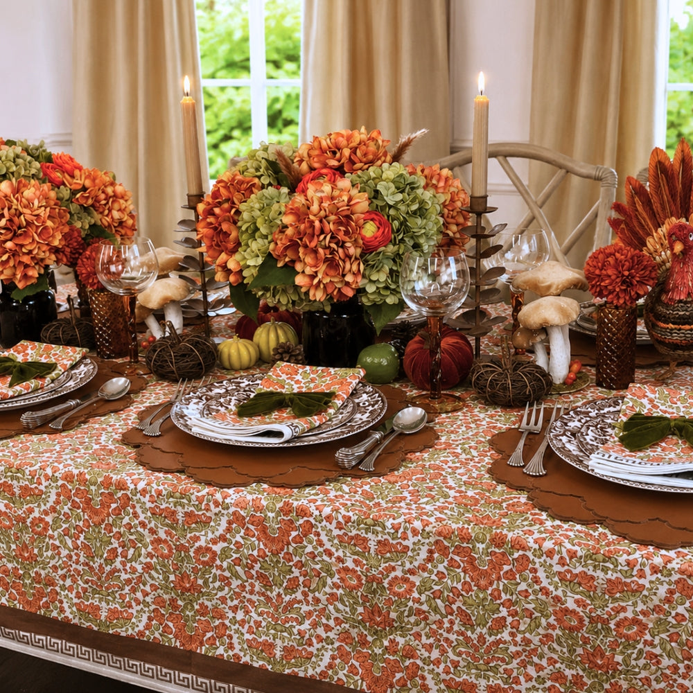 A hand block printed tablecloth, featuring a floral pumpkin and sage green floral pattern on a white background, finished with a brown band and Greek key border at the bottom, Thanksgiving tablecloth, luxury table linens