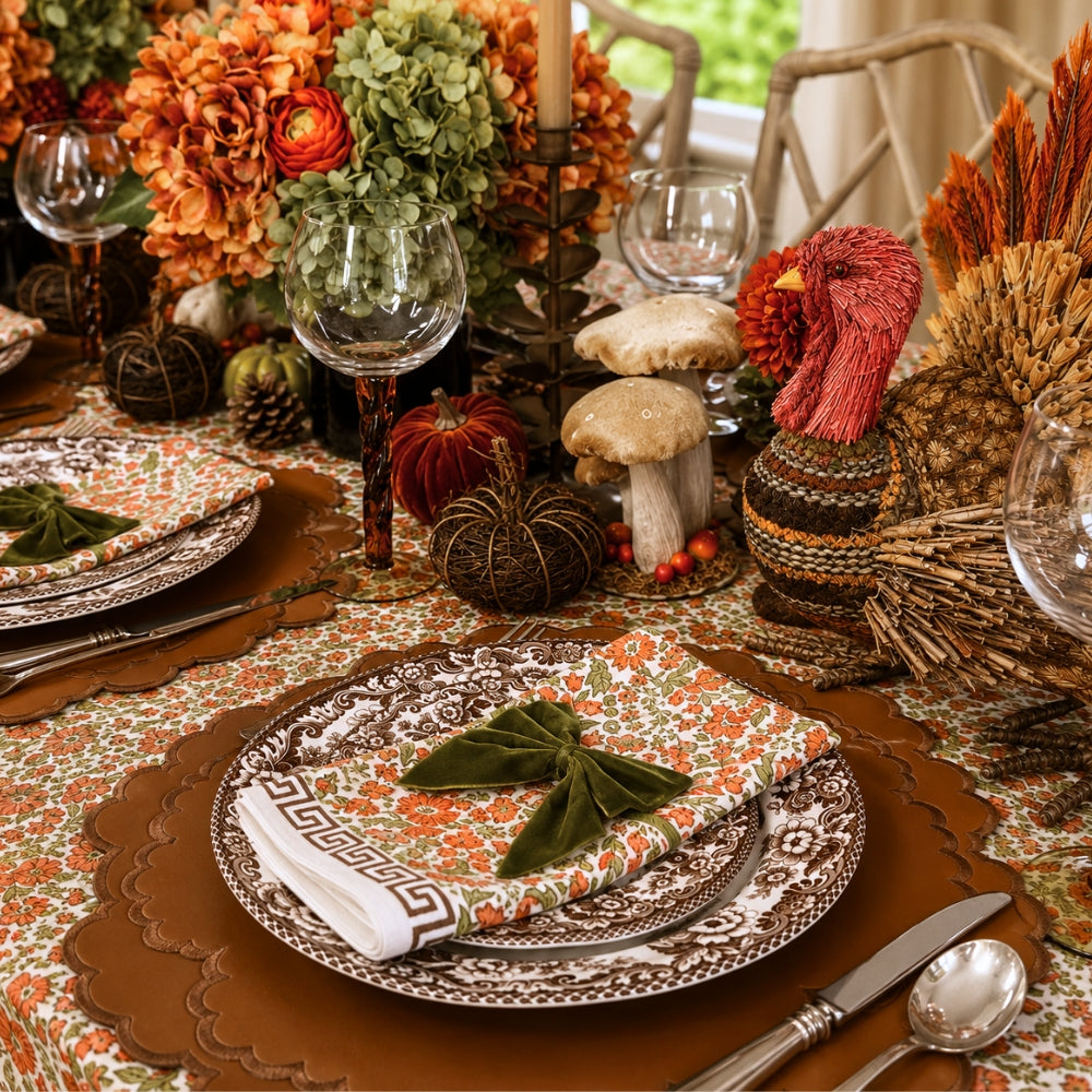 A hand block printed tablecloth, featuring a floral pumpkin and sage green floral pattern on a white background, finished with a brown band and Greek key border at the bottom, Thanksgiving tablecloth, luxury table linens