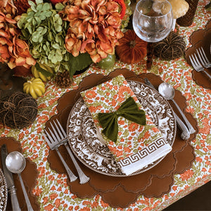 A hand block printed tablecloth, featuring a floral pumpkin and sage green floral pattern on a white background, finished with a brown band and Greek key border at the bottom, Thanksgiving tablecloth, luxury table linens