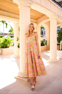 Woman in a floral dress standing in a sunlit outdoor setting with columns and plants.
