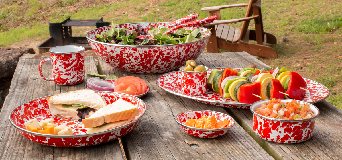 Red swirl enamel mug among matching picnic dinnerware on an outdoor picnic table