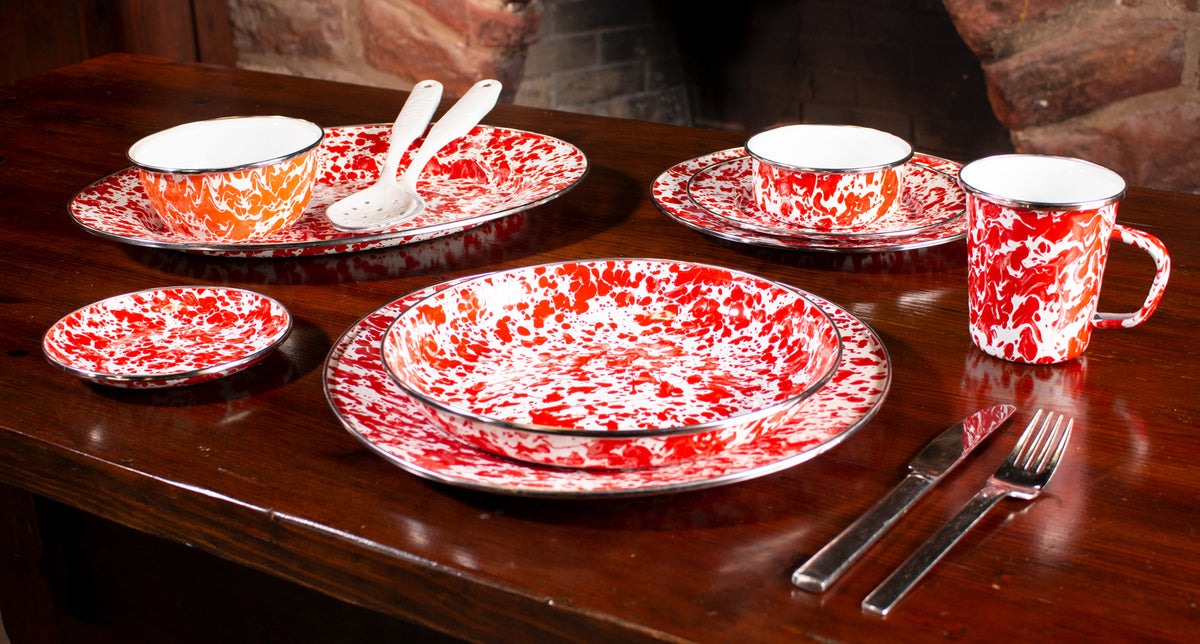 Angled view of Pasta Plates in Red Swirl, Set of 4 showcasing red-and-white enamel swirl on a wooden table