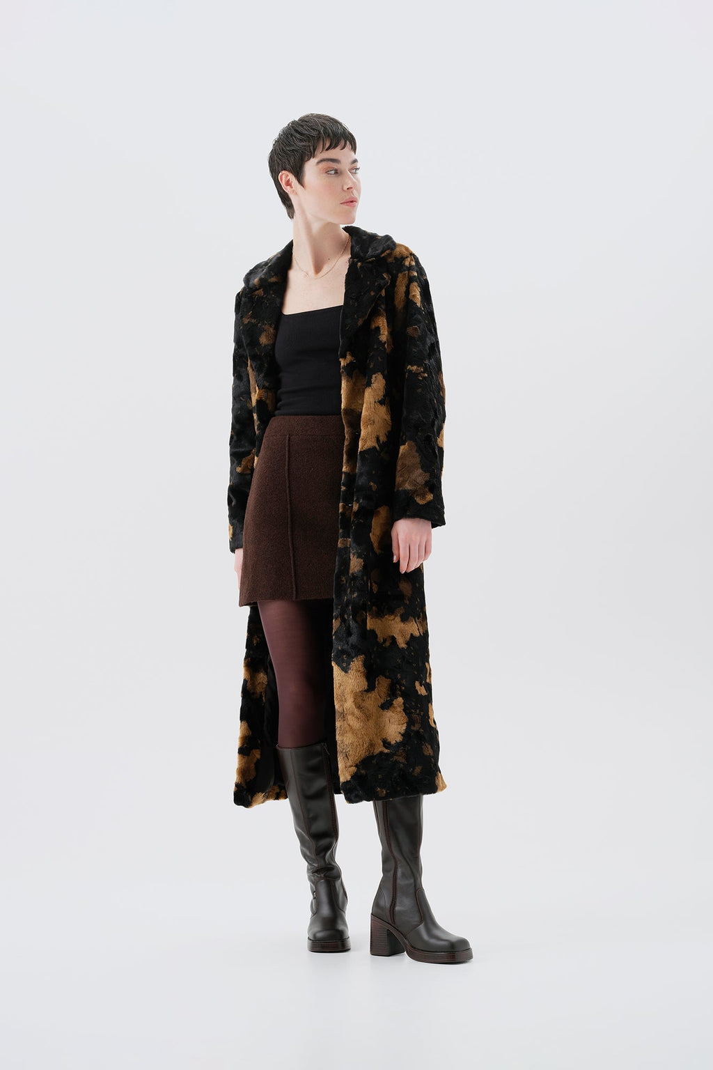 Model wearing a long black and brown faux fur coat with a cow pattern on a white background