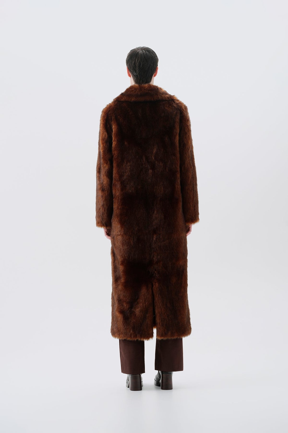 Model pictured from the back wearing a warm and long brown faux fur coat on a white background