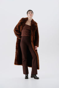 Model wearing a warm and long brown faux fur coat on a white background
