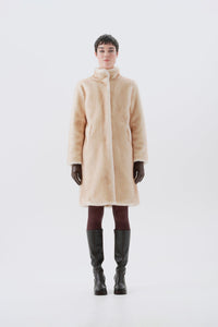 Model wearing a beige faux fur coat, dark pants, and black boots
