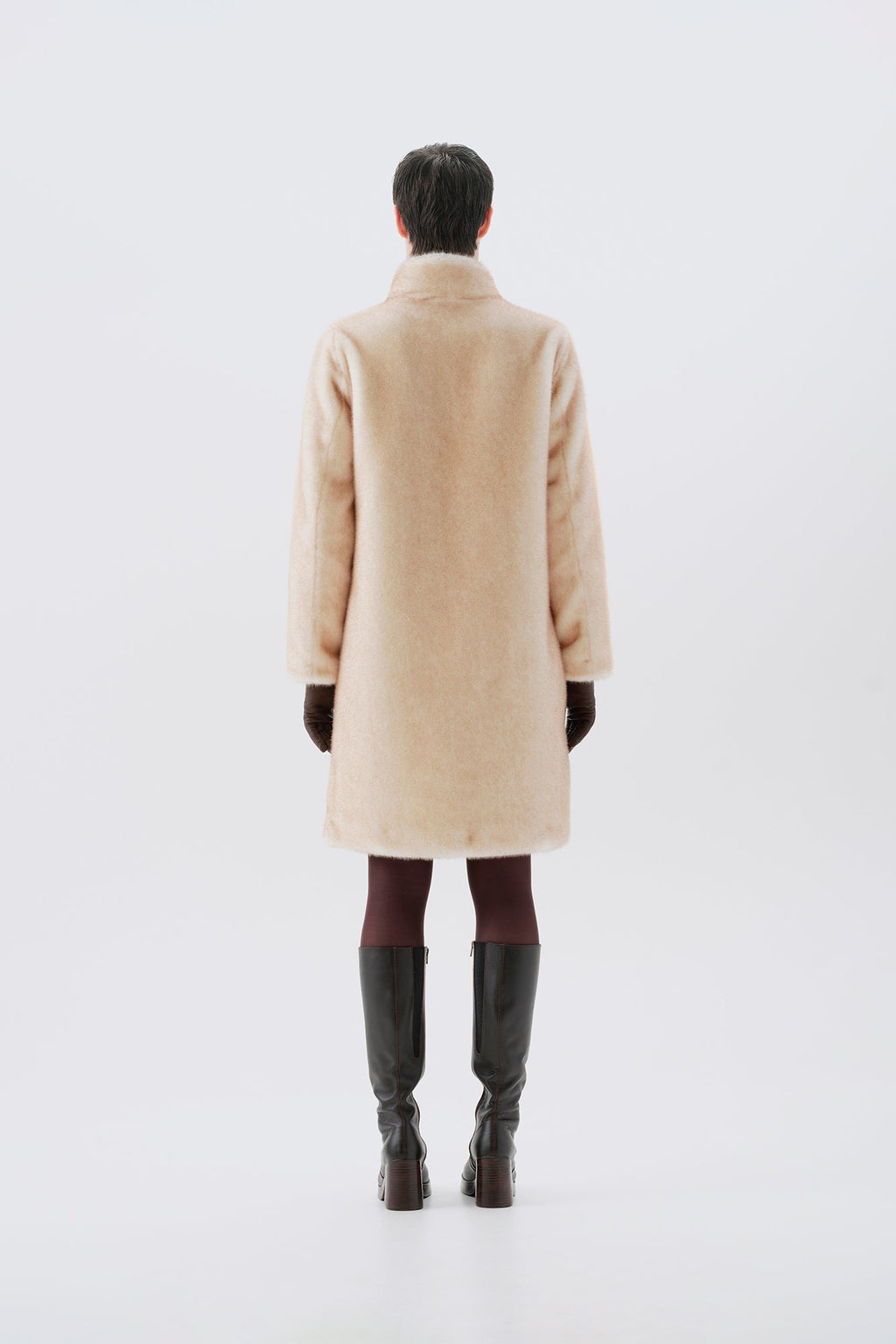 Model pictured from the back wearing a beige faux fur coat, dark pants, and black boots on a white background