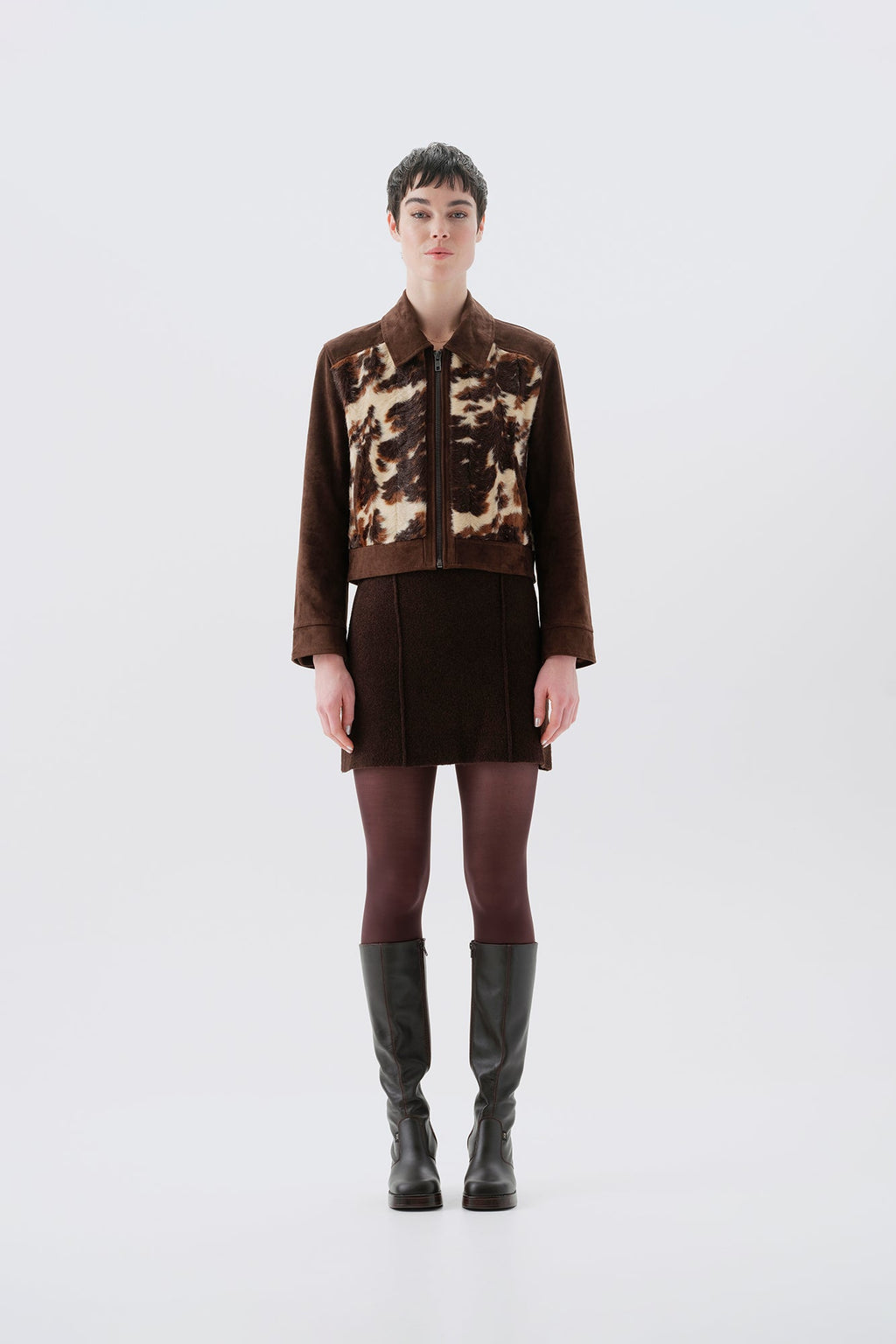 Model wearing a faux fur cow print jacket with brown vegan suede sleeves on a white background