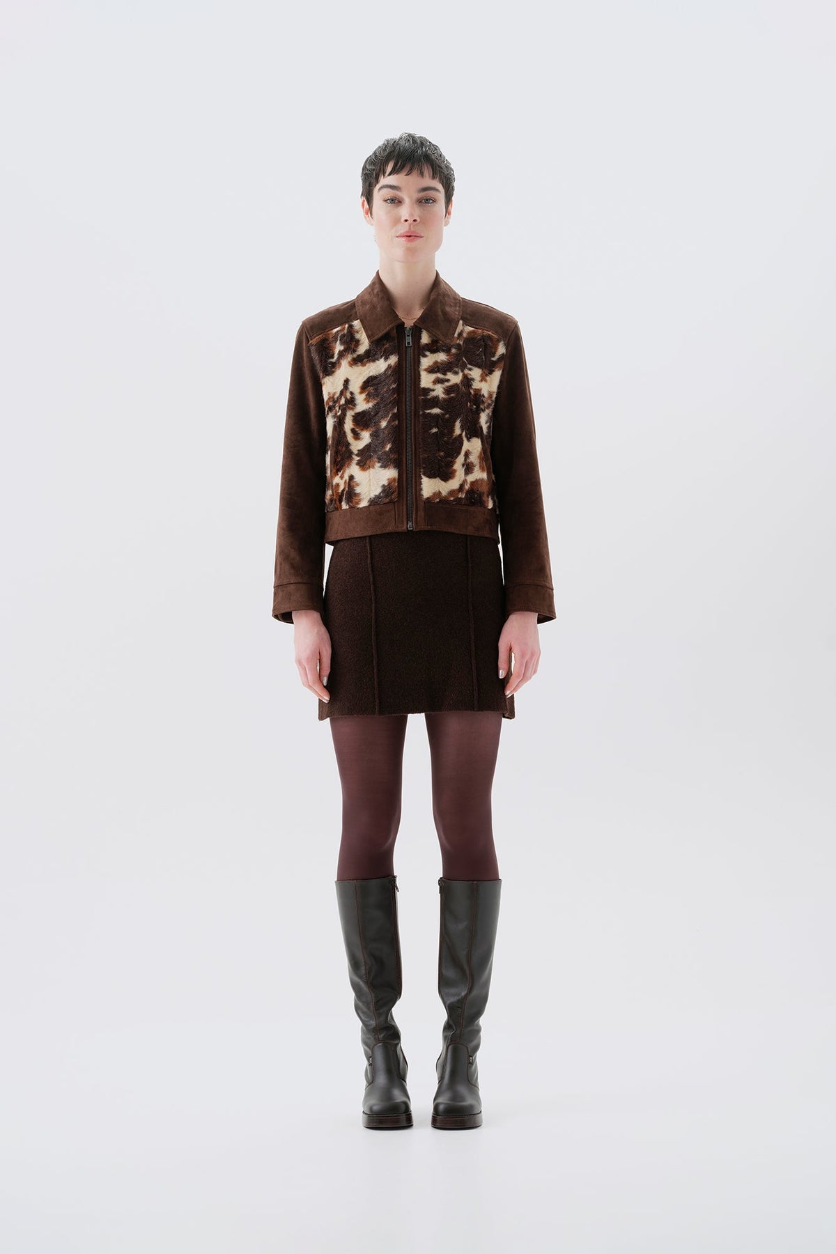 Model wearing a faux fur cow print jacket with brown vegan suede sleeves on a white background
