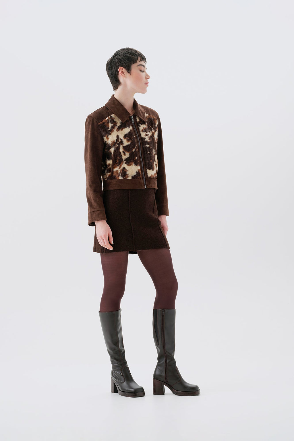 Model wearing a faux fur cow print jacket with brown vegan suede sleeves on a white background