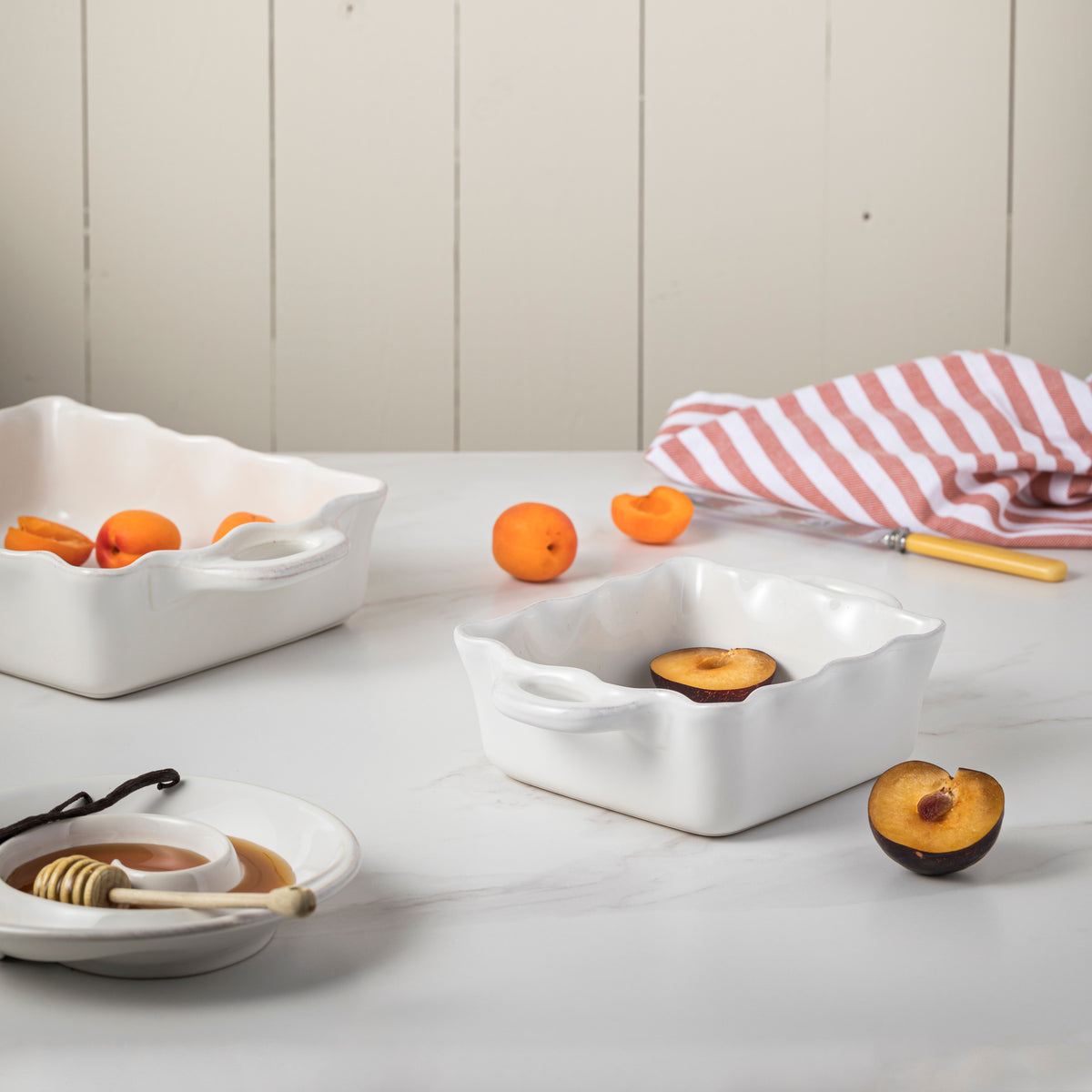 Angled view of Costa Nova Cook and Host Square Baker in White showcasing glossy glaze with fruit on a tabletop