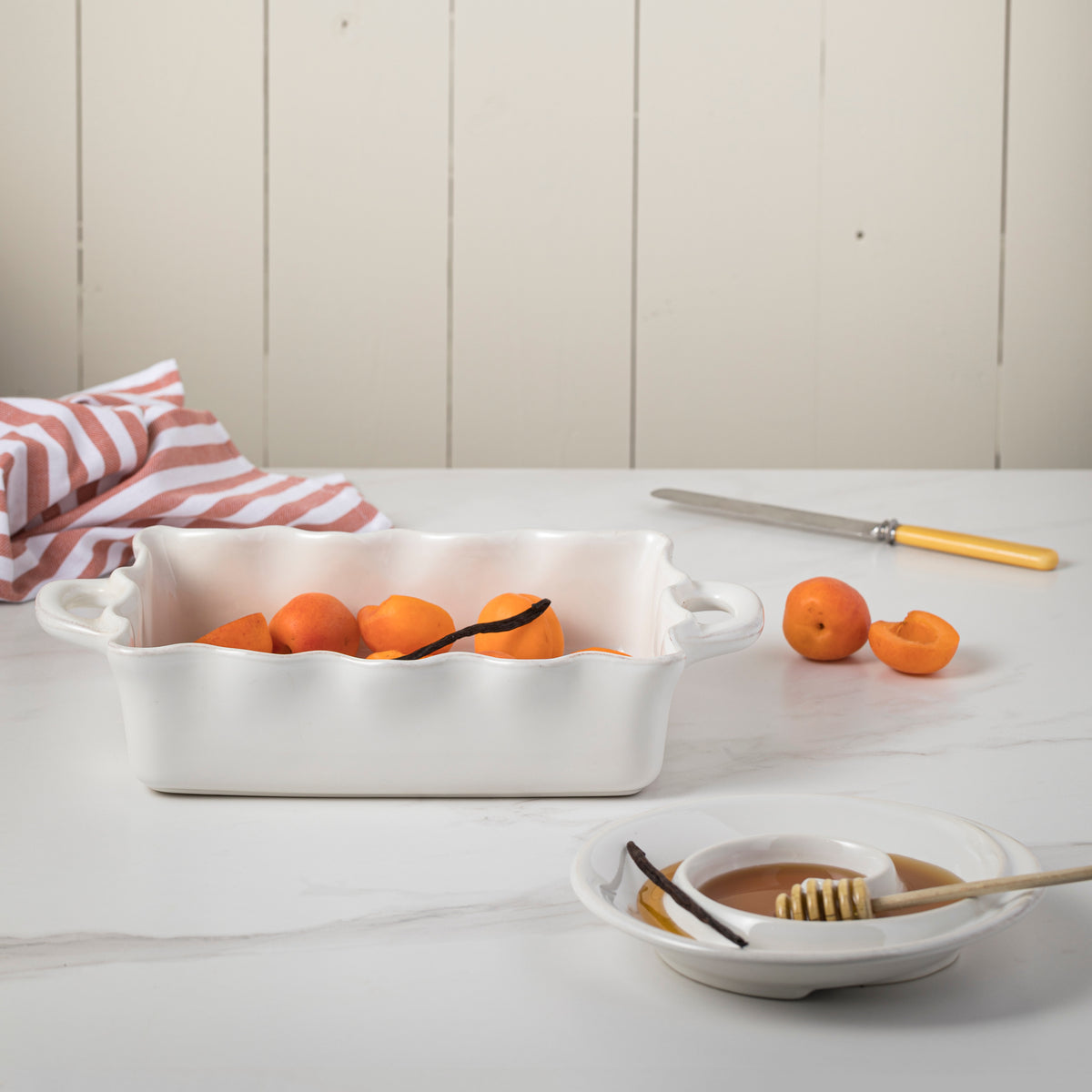 Front view of Costa Nova Rectangle Baker showcasing white glossy stoneware with apricots and honey on a kitchen counter
