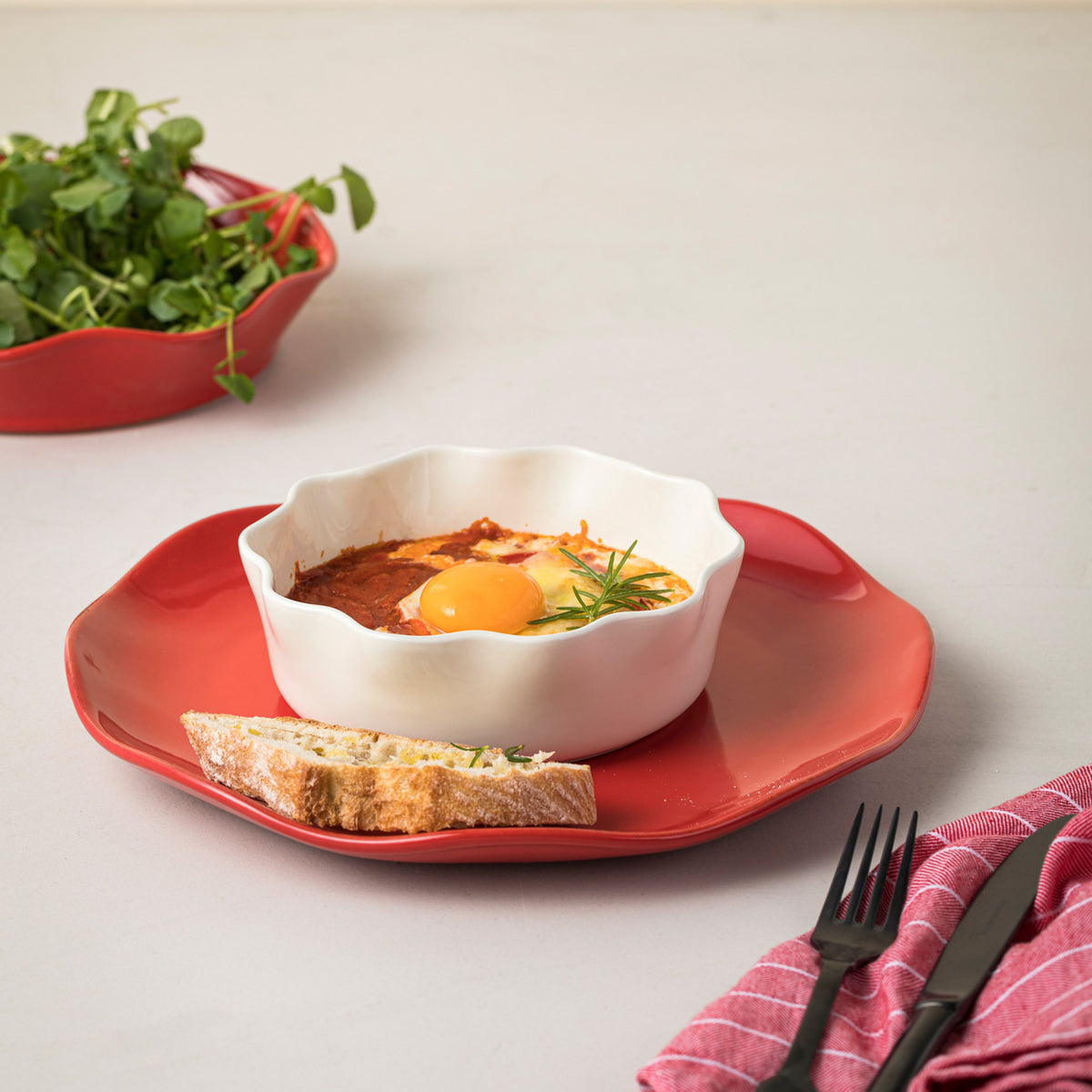 Three-quarter view of Costa Nova Cook and Host 7-inch white pie dish showing scalloped rim and glossy glaze on a red plate
