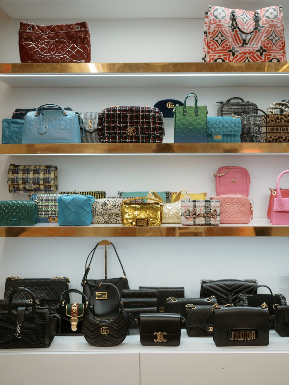 Assorted designer handbags displayed on white wall shelves with gold trim in a boutique
