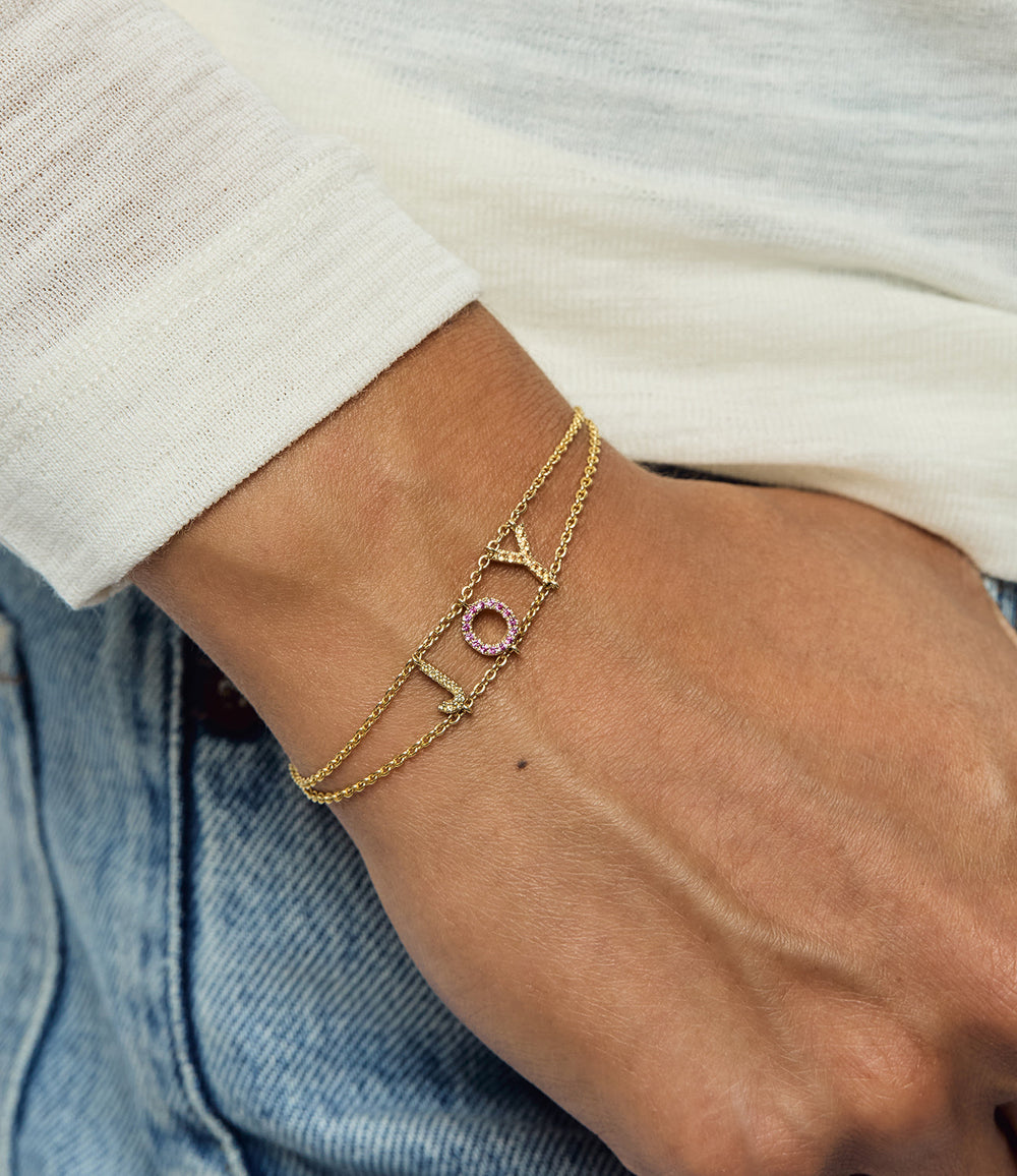 Close-up of wrist wearing Pink and Yellow Sapphire Joy bracelet showcasing gold double chains and JOY letter charms