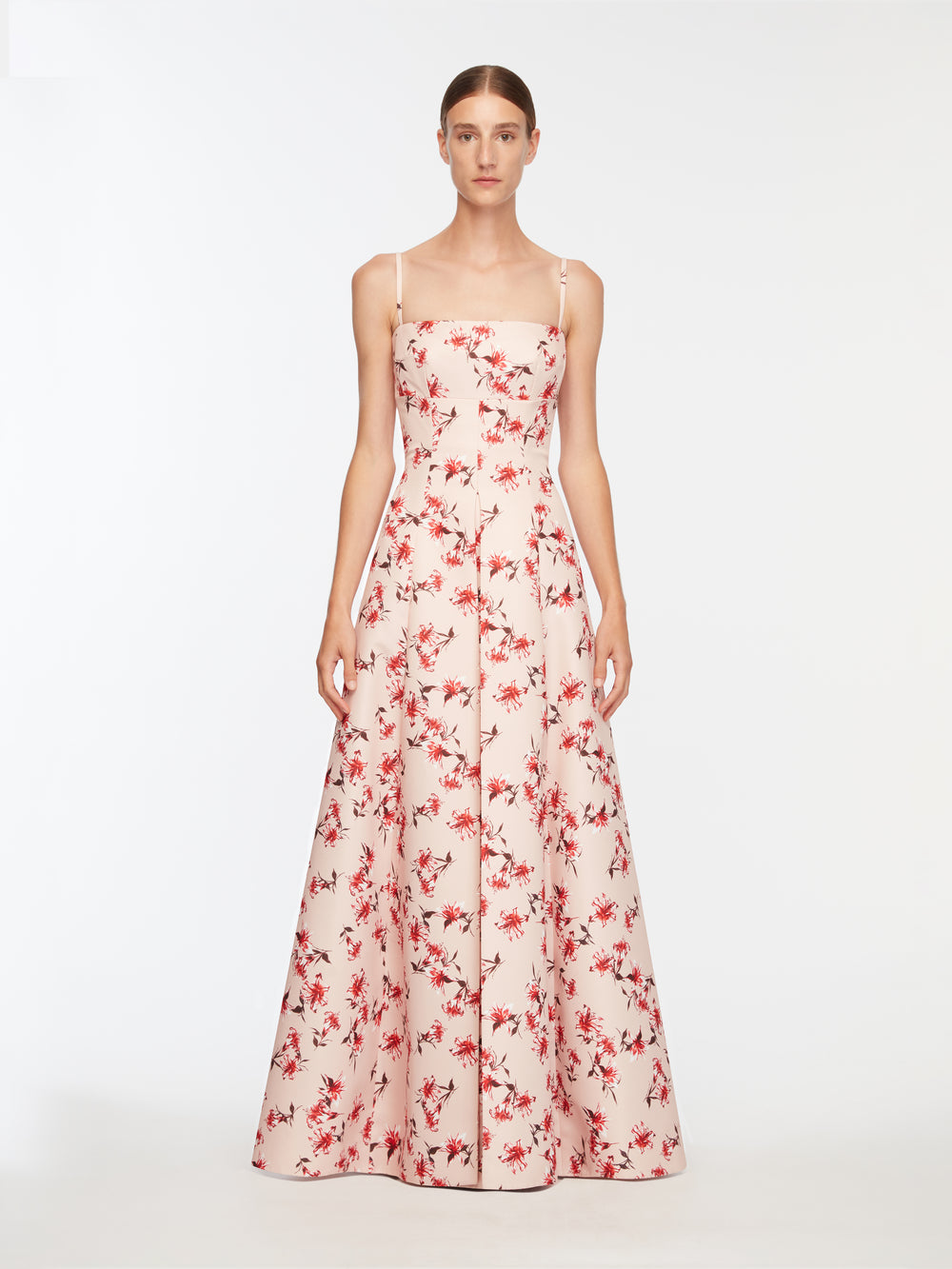 Front view of Oceana dress in pale pink with red floral Festive Lilies print, slim straps, fitted bodice and full A-line skirt on white background
