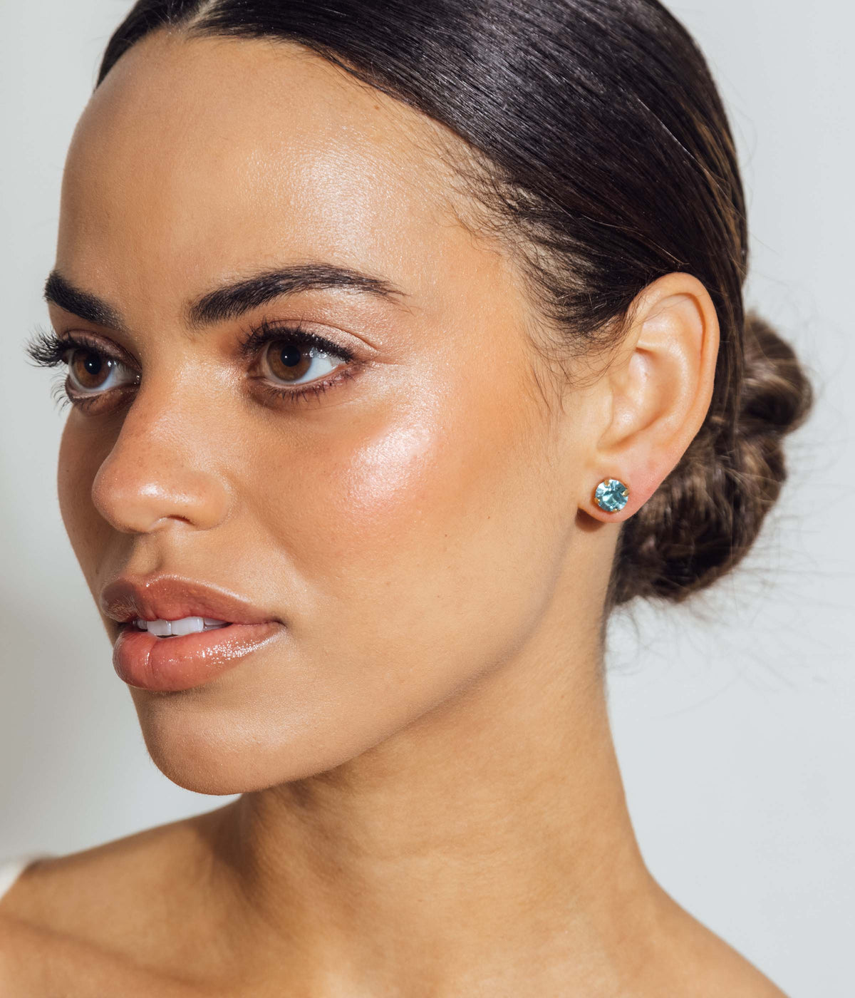 Close-up side view of model wearing Rainbow Bright stud set showing aqua crystal stud against a light neutral background