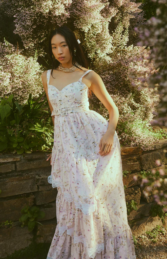 Front three quarter view of Reba Dress showcasing soft blush floral print, white crochet lace, and waist belt in a garden