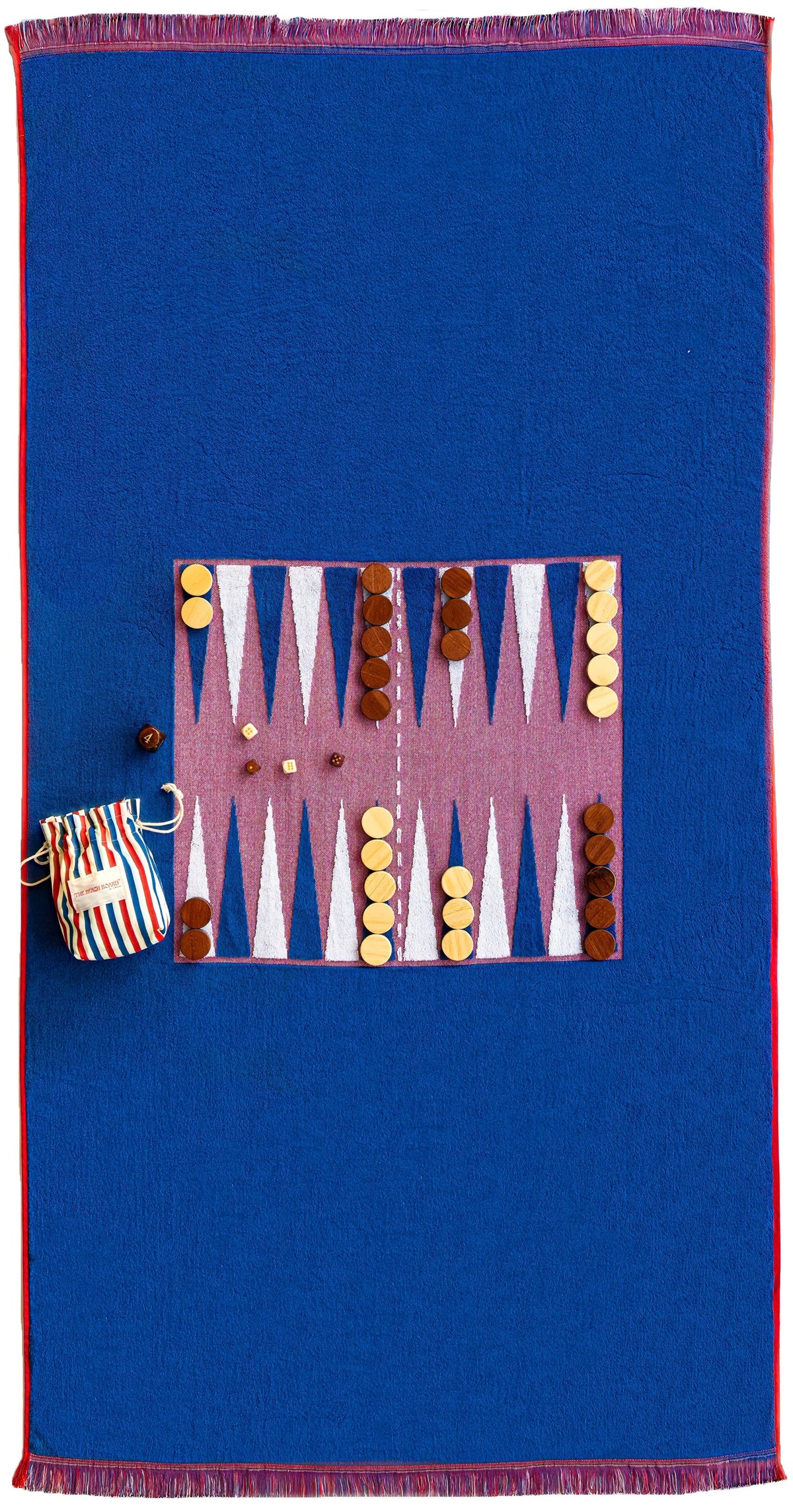 Top-down view of Nantucket Beach Board towel showing printed backgammon layout, wooden game pieces, and striped canvas pouch on blue terry with red trim