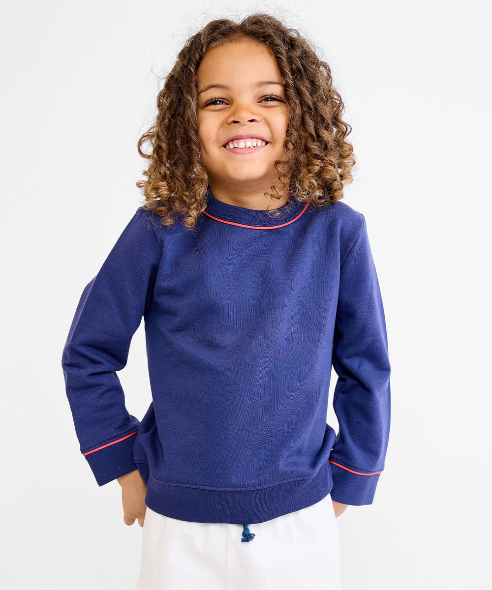 Front view of Remy sweatshirt in navy on child model showing contrast red piping at neckline and cuffs on white background