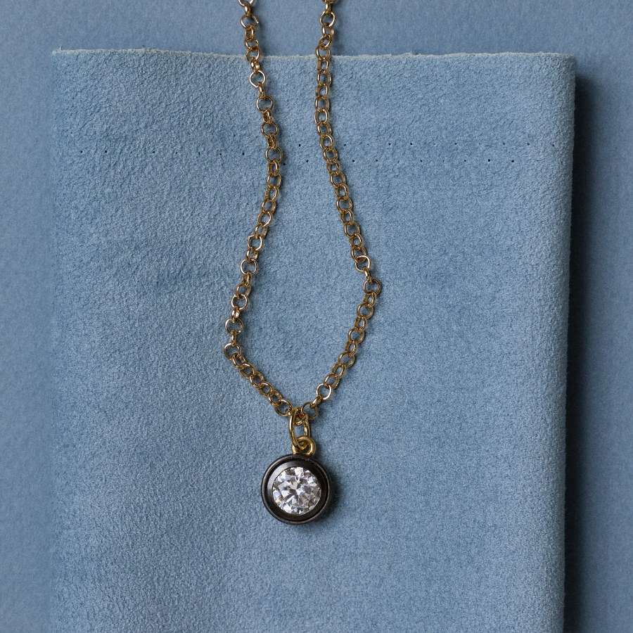 Front view of Rhodium Bezel Charm Necklace showcasing its round bezel charm with a blue fabric background