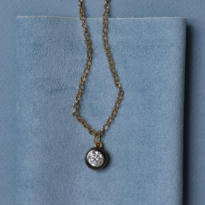 Front view of Rhodium Bezel Charm Necklace showcasing its round bezel charm with a blue fabric background