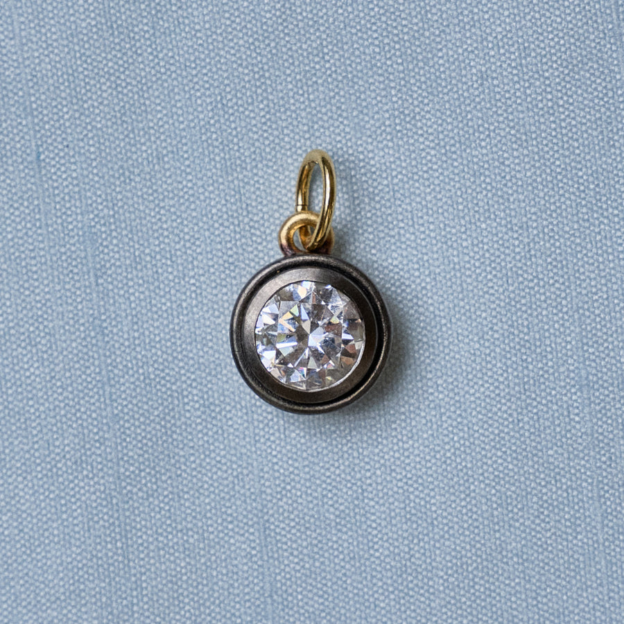 Close-up of Rhodium Bezel Charm Necklace pendant showcasing a round faceted centerpiece on blue fabric