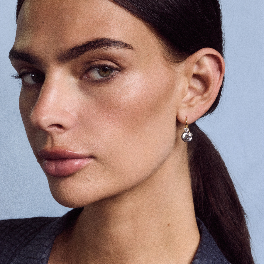 Close-up view of Rhodium Double Bezel Drop Earrings showcasing the double bezel drop design on a model against a blue background