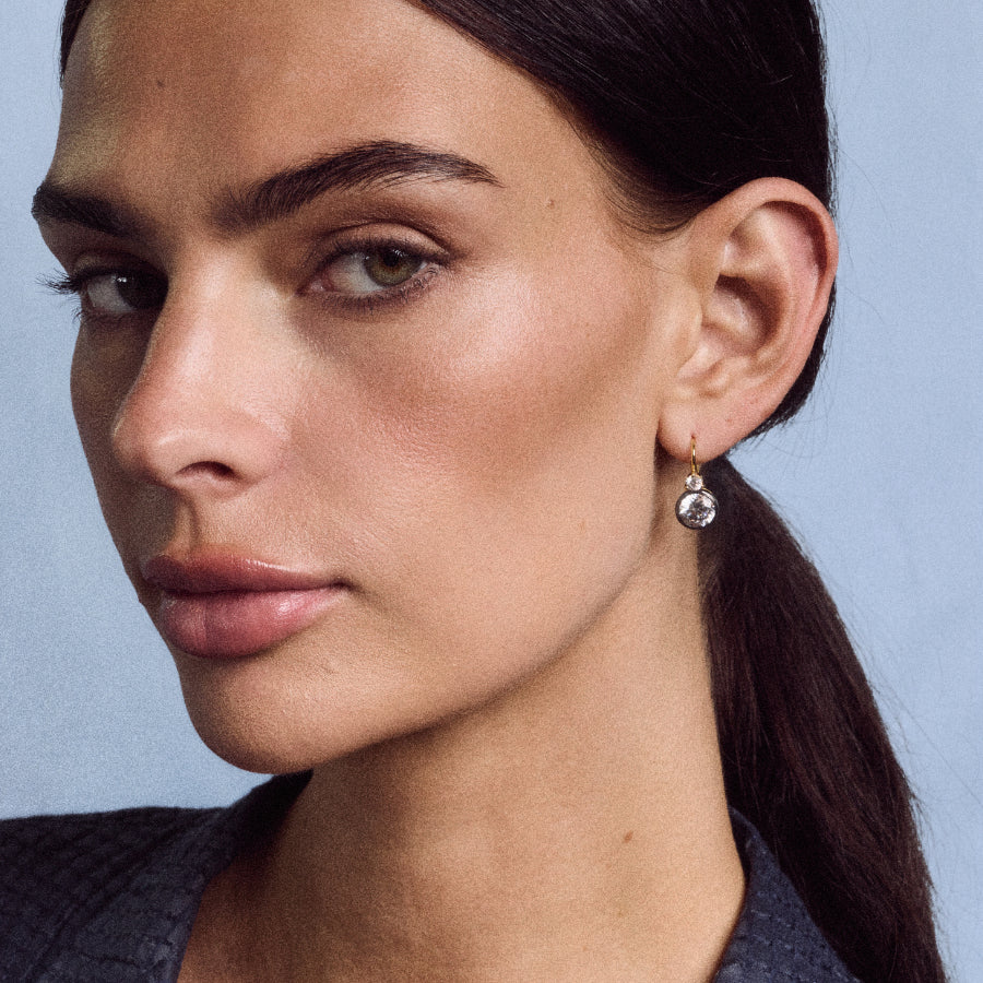 Close-up view of Rhodium Double Bezel Drop Earrings showcasing the double bezel drop design on a model against a blue background