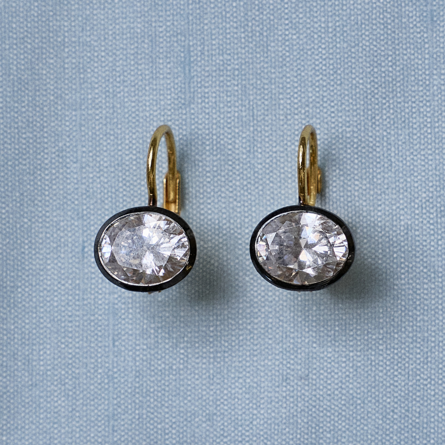 Front view of Rhodium Oval Bezel Drop Earrings showcasing oval stones in dark rhodium bezels on light blue fabric