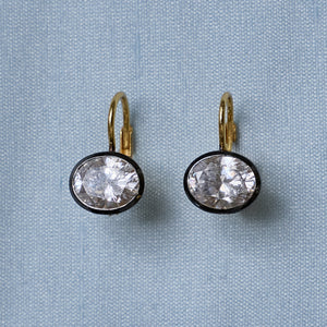 Front view of Rhodium Oval Bezel Drop Earrings showcasing oval stones in dark rhodium bezels on light blue fabric