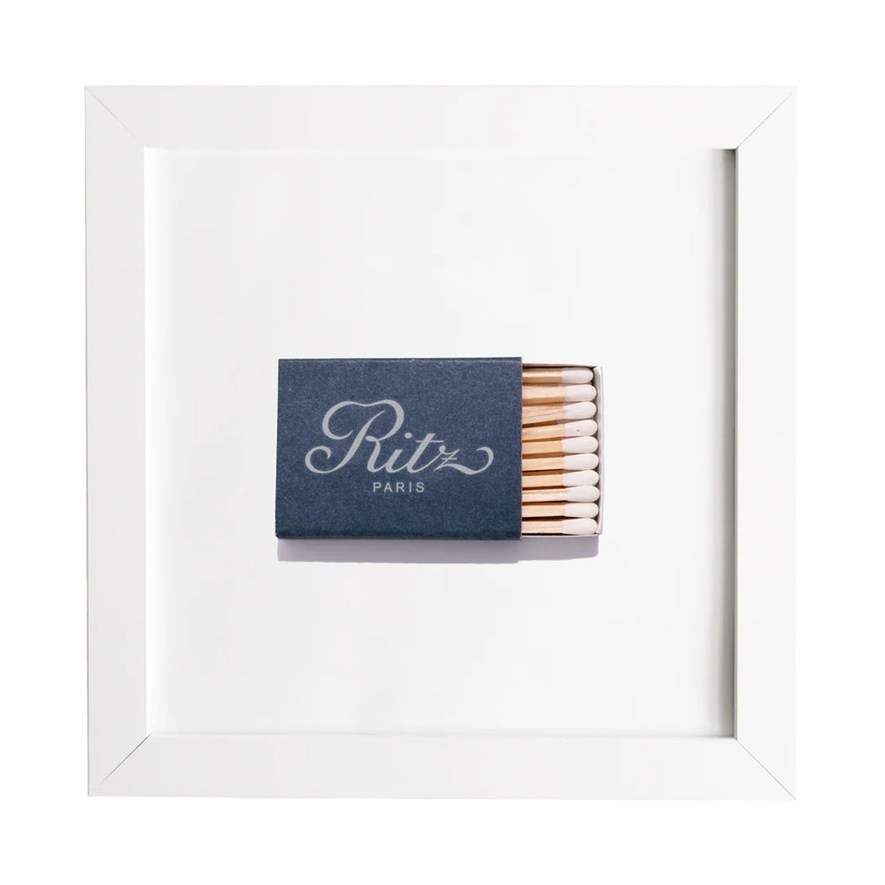 Straight-on view of framed Ritz Paris matchbook print showing navy matchbook centered in white frame on white background