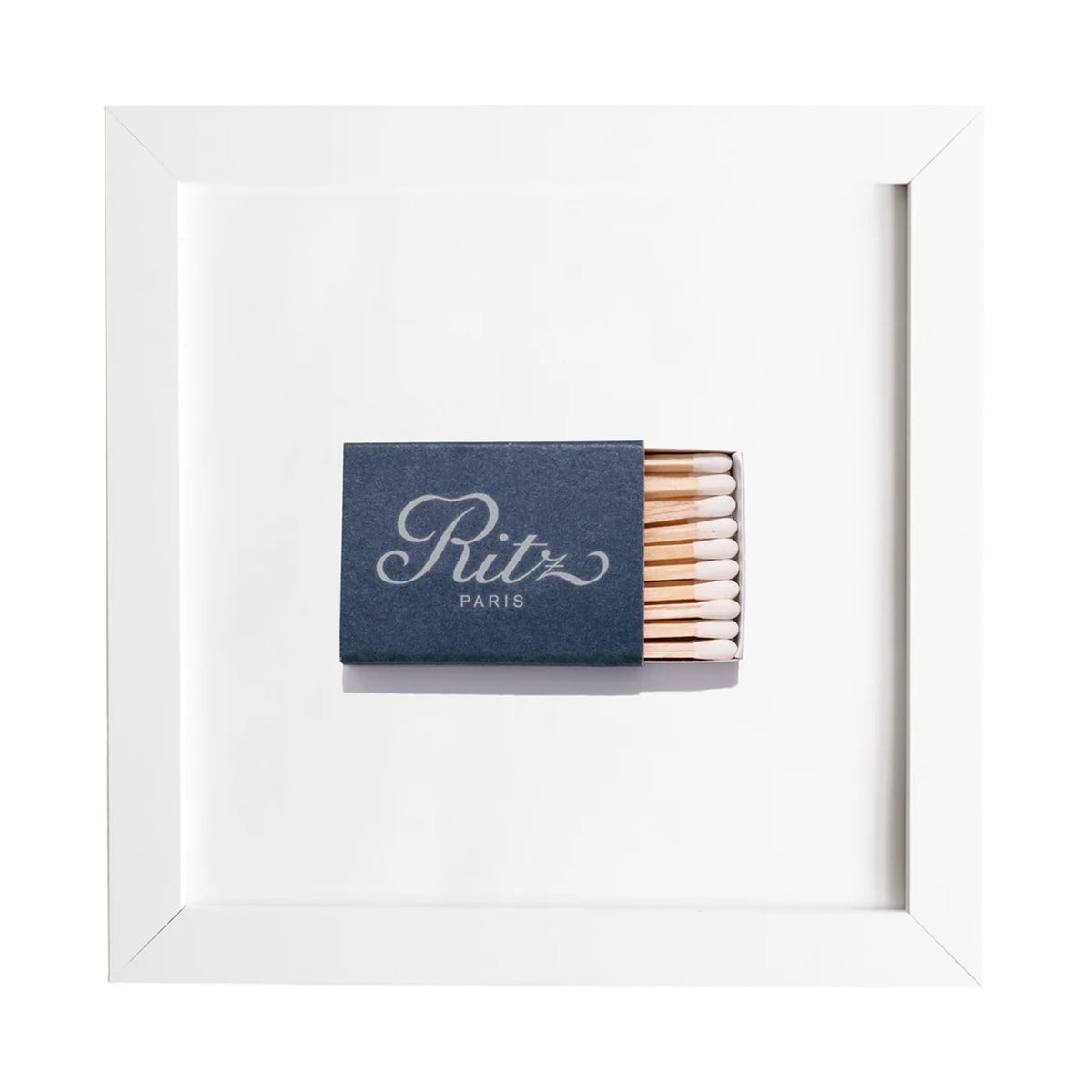Straight-on view of framed Ritz Paris matchbook print showing navy matchbook centered in white frame on white background