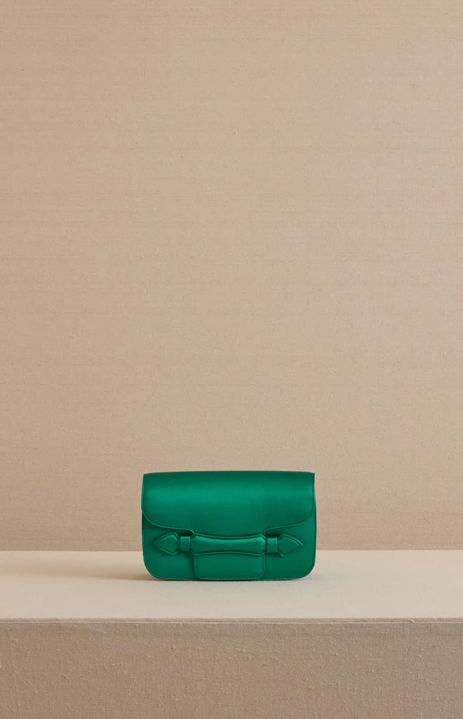 Front view of Romy clutch in satin emerald showcasing smooth satin exterior and curved flap on a beige pedestal