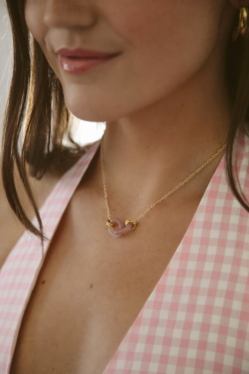 Close-up of Rose Rings Necklace on model showing two rose quartz interlocking rings on gold rope chain at collarbone