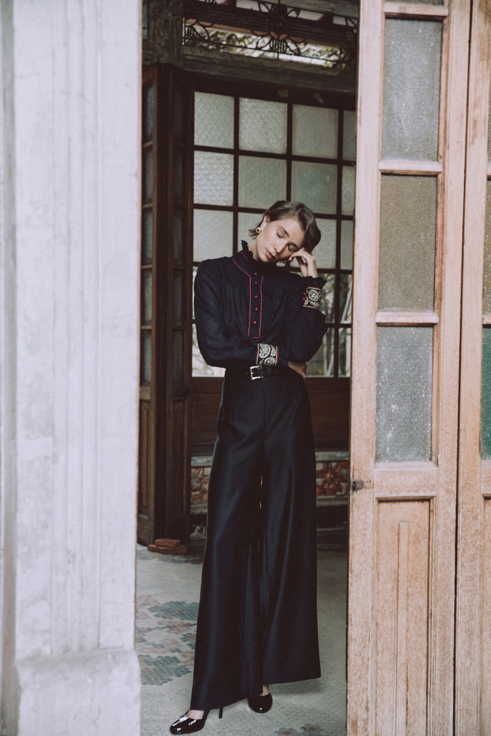 Front full-length view of Raha pants in black silk showcasing high-waisted wide-leg silhouette on a model in a doorway
