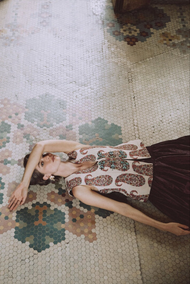High-angle view of Roya Vest on model showcasing paisley Termeh fabric and hand-embroidered beaded motifs on a mosaic-tile floor