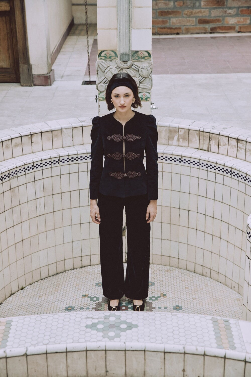 Front view of Mahtab straight-leg velvet pants in black on model showcasing high waist and straight-leg silhouette in a tiled basin setting