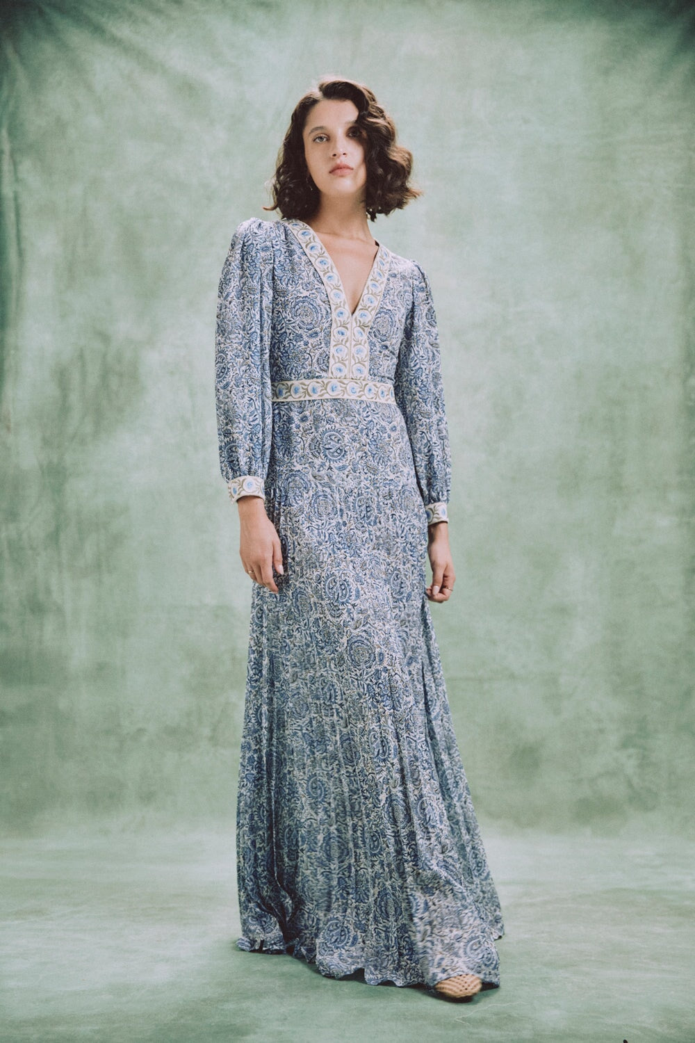 Front view of Tooba maxi dress in blue chiffon with V-neck embroidery, long sleeves and pleated skirt on green backdrop