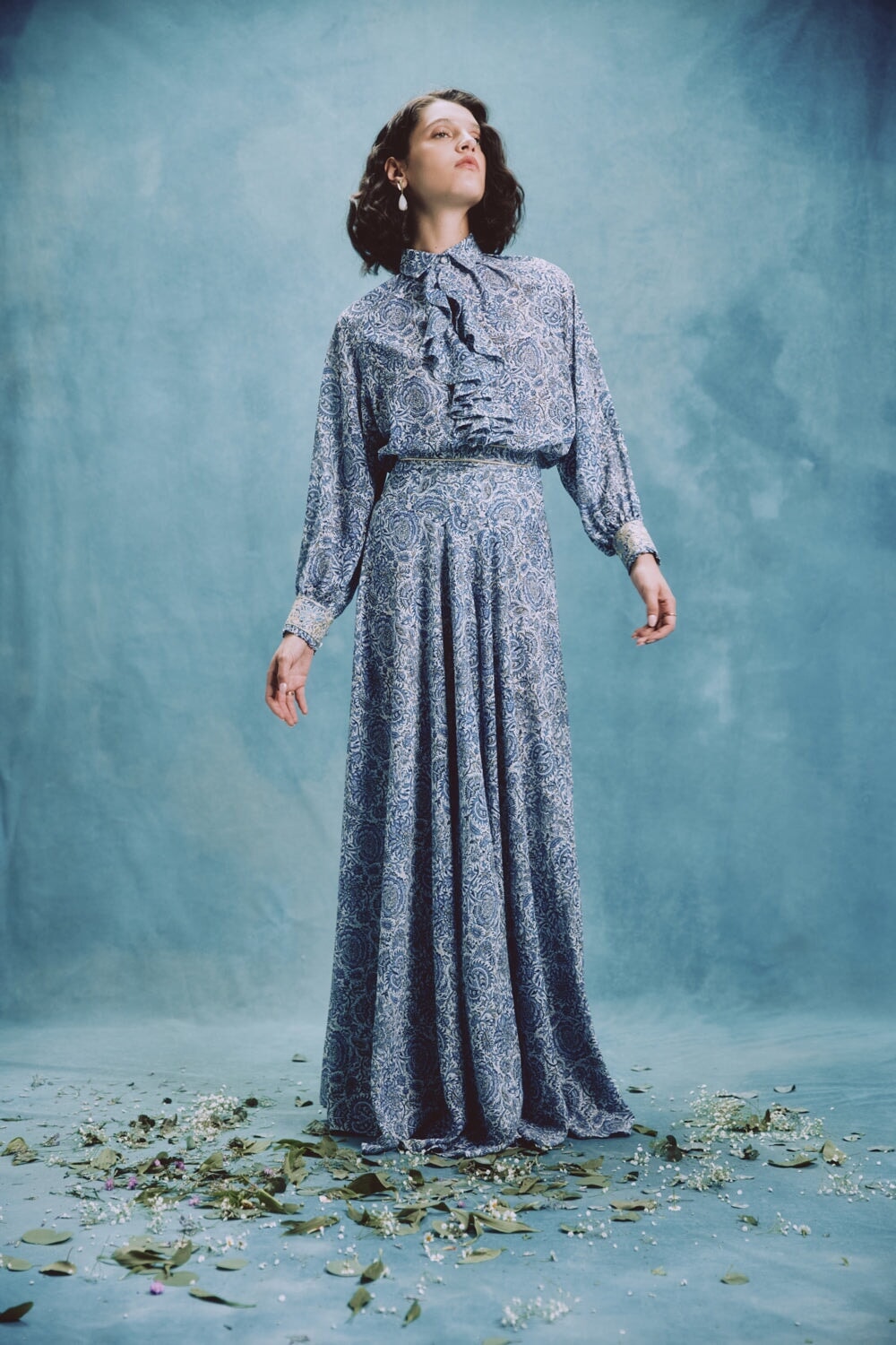 Front view of Naz Blouse on model in blue chiffon with ruffled neckline, paired with matching maxi skirt on blue backdrop