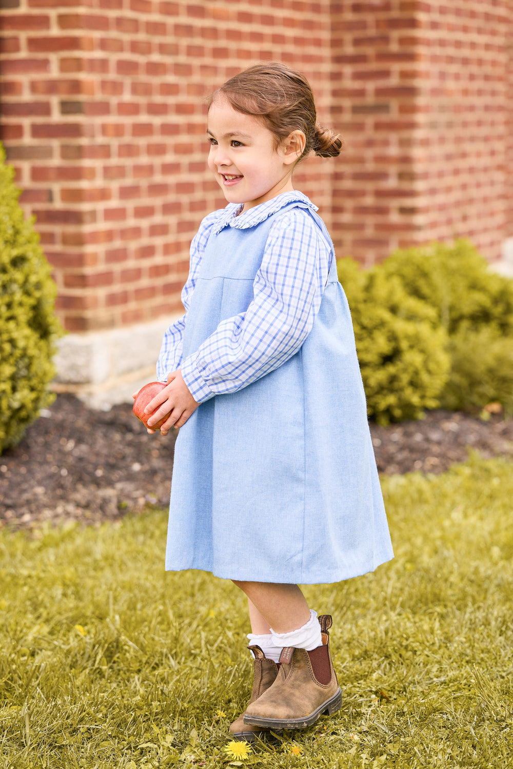 Side view of blue Charleston jumper over light blue plaid Peter Pan blouse, ruffled collar on toddler by brick wall