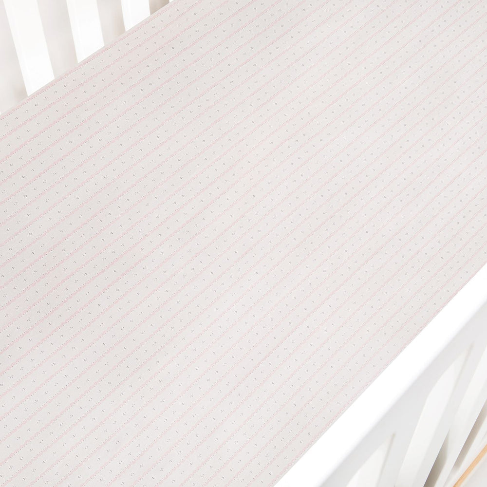 Top-down view of Petal Scallops crib sheet in pink showing diagonal scallop-stripe pattern in a white crib