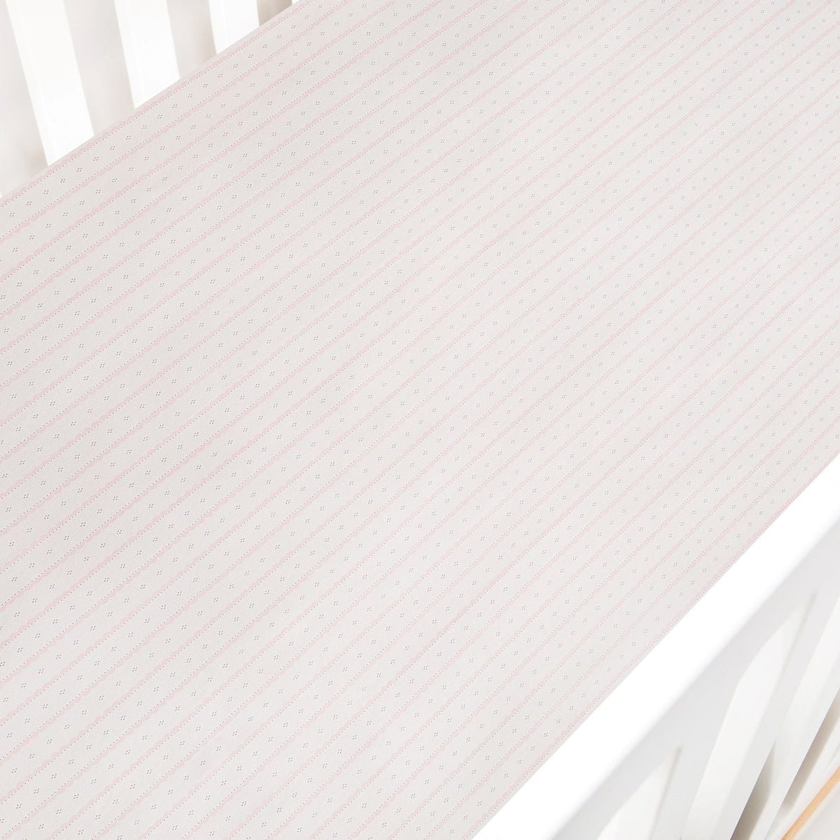 Top-down view of Petal Scallops crib sheet in pink showing diagonal scallop-stripe pattern in a white crib