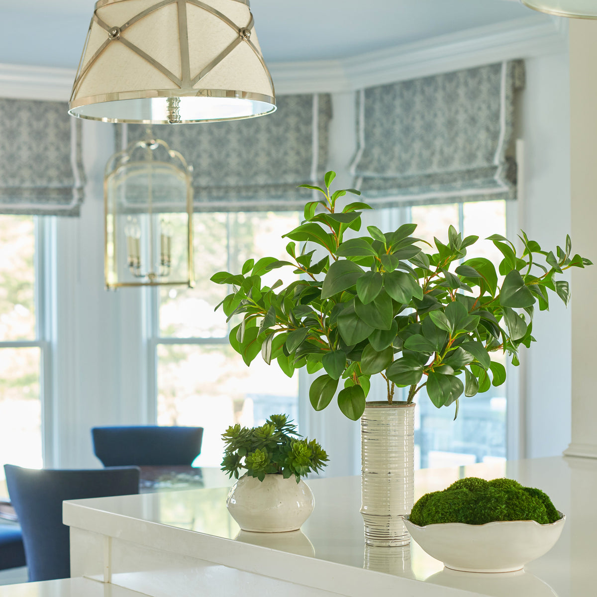 Front view of Mossy Mood faux green foliage arrangement in tall ribbed ceramic vase on white kitchen island