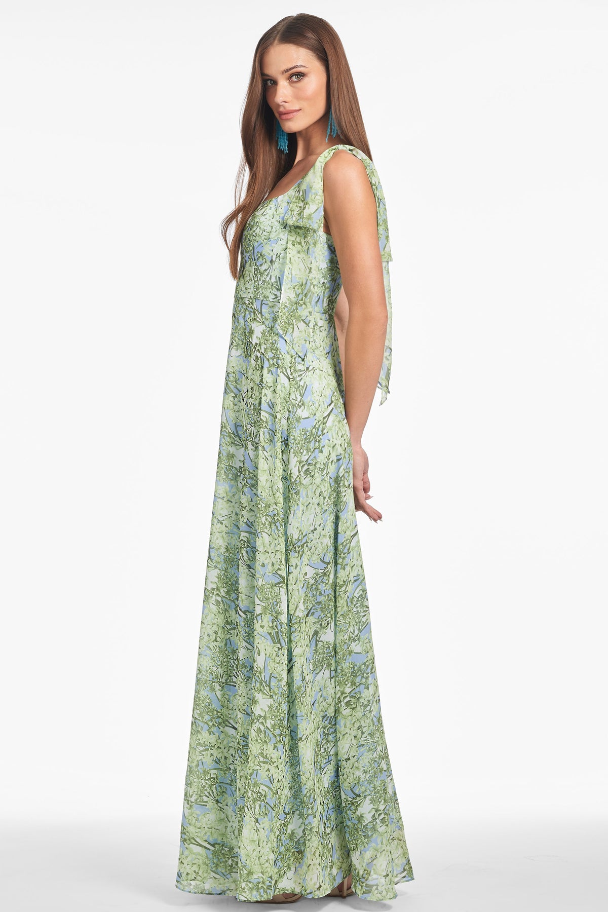 Side view of Pearl Gown in Peridot Bouquet on model showcasing tied shoulder straps and flowing floor-length chiffon skirt on white background