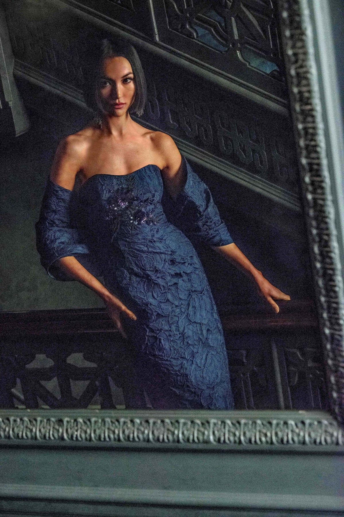 Front view of Edie Gown in Deep Ocean Bouquet showcasing strapless sweetheart neckline and floral bodice on a dark sofa