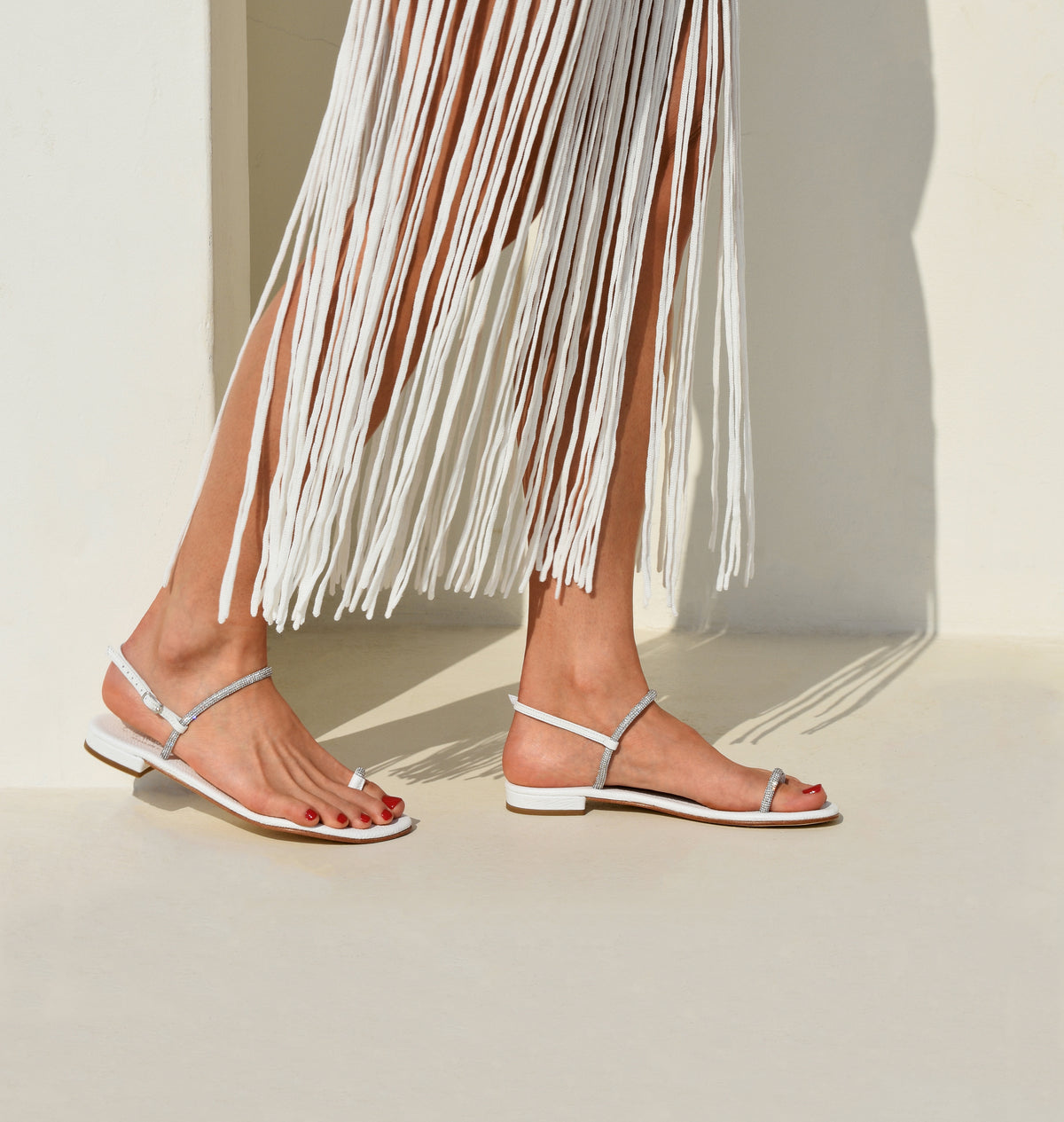 Side view of Sardinia sandal in white with rhinestone straps, toe loop, and low stacked heel on model in sunlit neutral setting