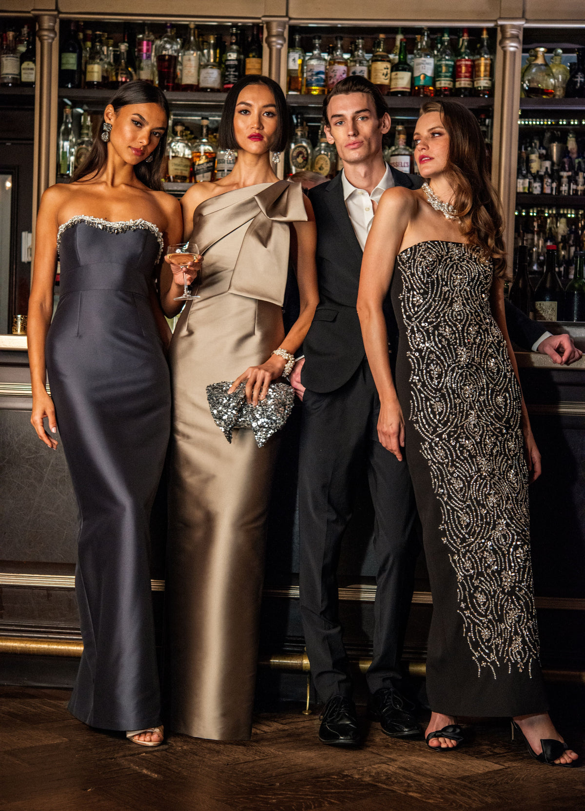 Front view of Hedy Gown in charcoal showcasing strapless silhouette and embellished sweetheart neckline, model at a bar