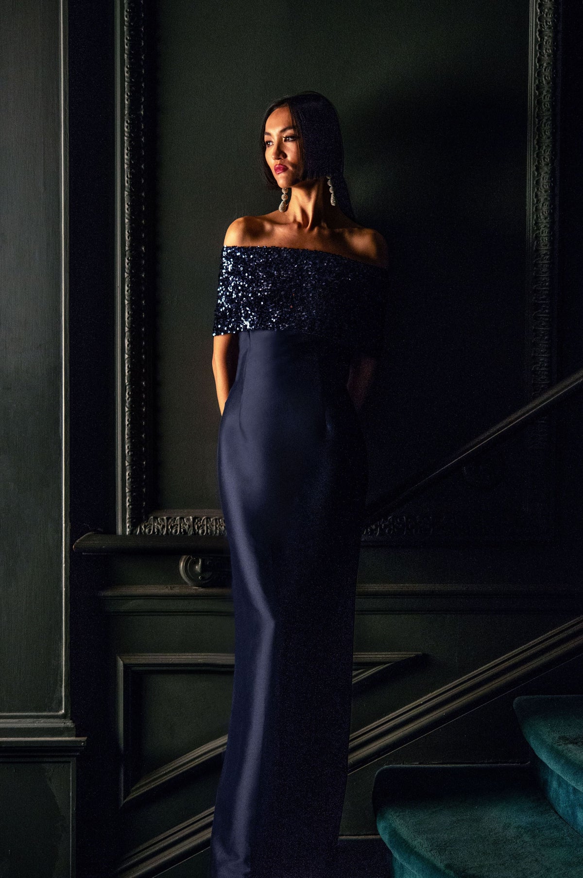 Three-quarter view of Ada Gown in Poseidon Night Sky showcasing its sequin fold-over neckline with a dark ornate background